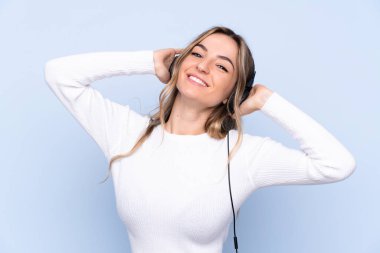 Soyutlanmış mavi arka planda müzik dinleyen genç bir kadın.