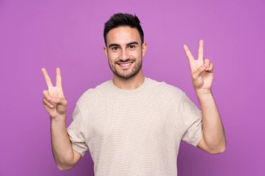 Mor arka planda kalan yakışıklı genç adam iki eliyle zafer işareti gösteriyor.
