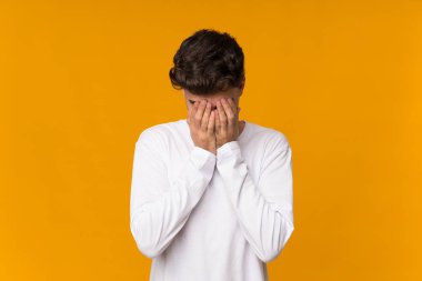 Genç adam turuncu arka planda, yorgun ve hasta bir ifadeyle.