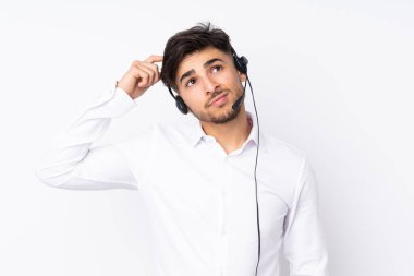 Tele pazarlamacı Arap bir adam beyaz arka planda izole edilmiş bir kulaklıkla çalışıyor. Şüpheleri var ve kafası karışmış bir yüz ifadesi var.