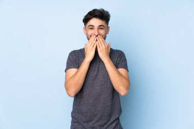 Arap yakışıklı adam izole edilmiş arka planda mutlu ve gülümsüyor elleriyle ağzını kapatıyor.