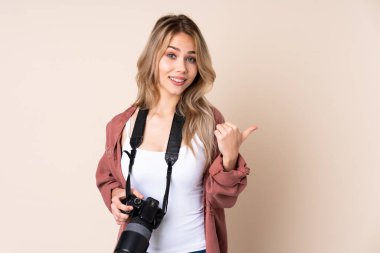 İzole edilmiş arka planda genç fotoğrafçı kız bir ürünü sunmak için kenarı işaret ediyor.