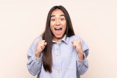 Kazanan pozisyondaki zaferi kutlayan bej arka planda izole edilmiş genç Hintli kadın.