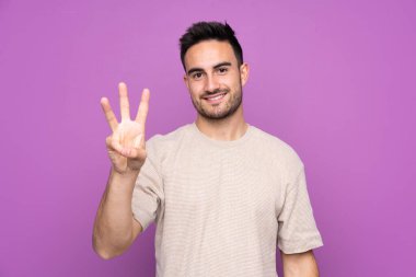 Soyutlanmış mor bir geçmişi olan yakışıklı bir adam mutlu ve parmaklarıyla üçe kadar sayıyor.