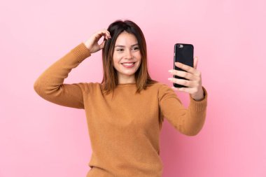 Soyutlanmış pembe arka planı olan genç bir kadın selfie çekiyor.