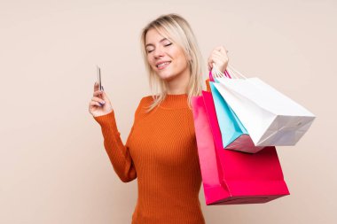 Soyutlanmış bir geçmişi olan genç sarışın bir kadın alışveriş torbaları ve bir kredi kartı tutuyor.