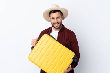 Seyahat çantası ve şapkasıyla izole edilmiş beyaz bir geçmişi olan genç yakışıklı bir adam.