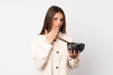 Beyaz arka planda izole edilmiş beyaz tenli genç bir kız elinde çubuklu bir kase erişte tutuyordu ve şaşırmıştı.