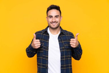 Izole sarı arka plan üzerinde genç yakışıklı adam jest kadar bir başparmak veren