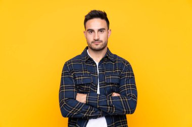 Izole sarı arka plan üzerinde genç yakışıklı adam kollarını çapraz tutmak