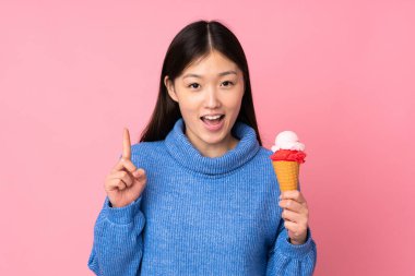 Kornet dondurmalı genç Asyalı kadın pembe arka planda izole edilmiş harika bir fikre işaret ediyor.