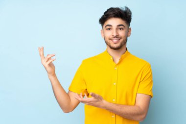 Arap yakışıklı adam soyutlanmış arka planda. Davet edilmek için ellerini yana uzatıyor.