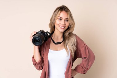 Genç fotoğrafçı kız izole edilmiş, kolları kalçasında ve gülümseyerek poz veriyor.