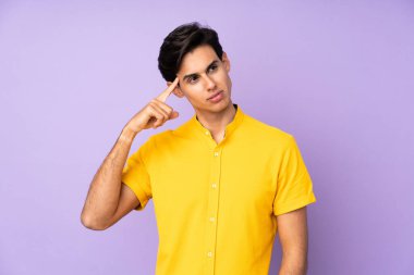 İzole edilmiş mor arka planı olan bir adam deliliğin jestini yapıyor. Parmağını kafaya koyuyor.