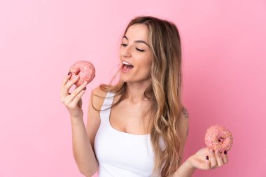 Soyutlanmış pembe arka planı olan genç bir kadın elinde mutlu bir ifadeyle donut tutuyor.