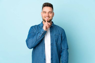 Mavi arka planda izole edilmiş Rus yakışıklı bir adam sessizlik işareti gösteriyor. Parmağını ağzına sokuyor.