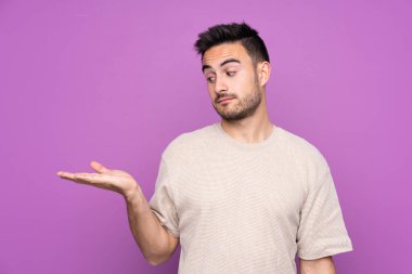 İzole edilmiş mor arka planı olan yakışıklı bir genç. Kopyalama alanını şüphelerle dolduruyor.