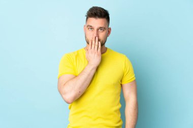 Rus yakışıklı adam mavi arka planda tek başına ağzını eliyle kapatıyor.