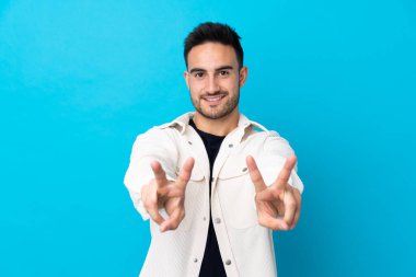 Mavi arka planda genç yakışıklı adam gülümsüyor ve zafer işareti gösteriyor.