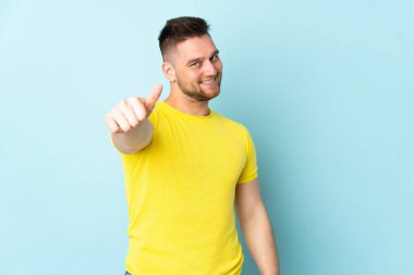 Rus yakışıklı adam mavi arka planda izole edildi. Başparmakları havada çünkü iyi bir şey oldu.