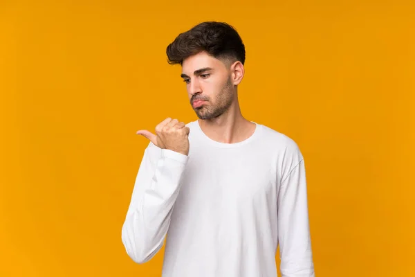 Junger Mann Vor Orangefarbenem Hintergrund Unglücklich Und Zeigt Zur Seite — Stockfoto