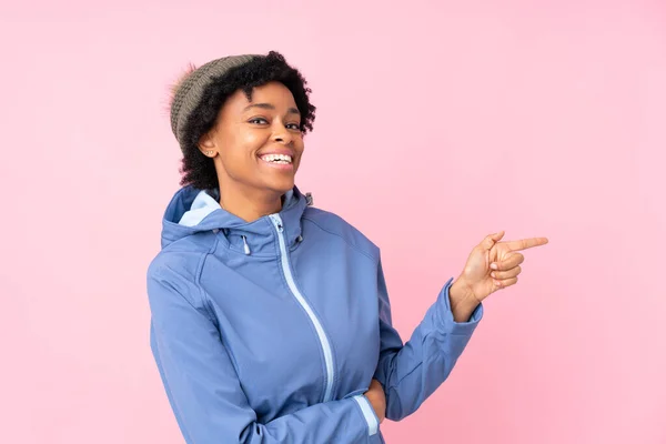 非洲裔美国妇女 头戴冬季帽 孤立的粉色背景 手指指向侧面 — 图库照片