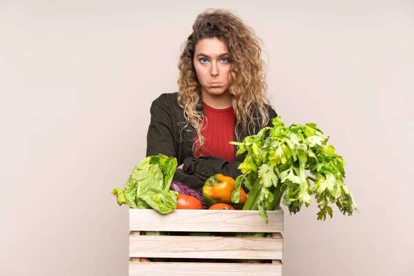 Farmer with freshly picked vegetables in a box isolated on beige background sad