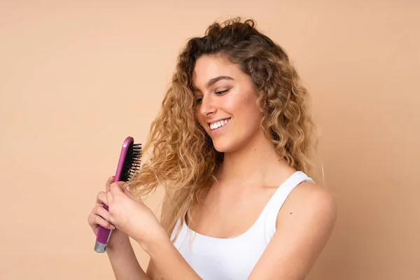 Young blonde woman with curly hair isolated on beige background with hair comb