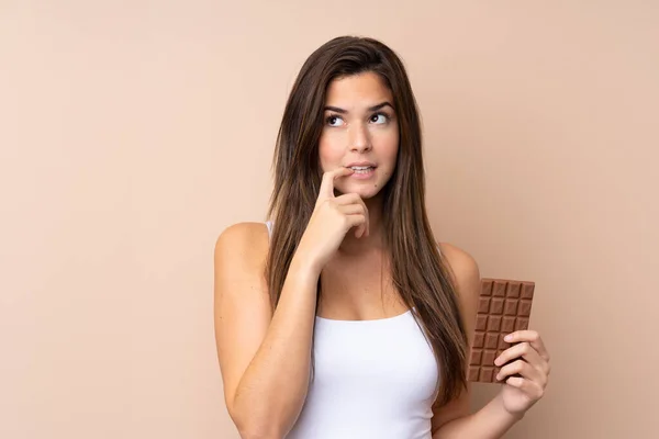 Teenager Dívka Přes Izolované Pozadí Čokoládovou Tabletu Mají Pochybnosti — Stock fotografie