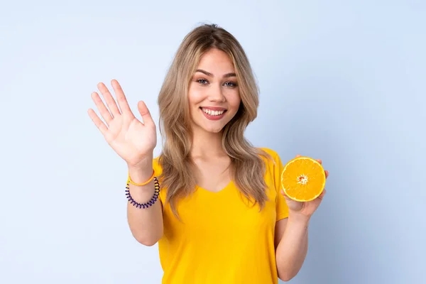 Teenager Russian Girl Holding Orange Isolated Blue Background Saluting Hand — Stock Fotó