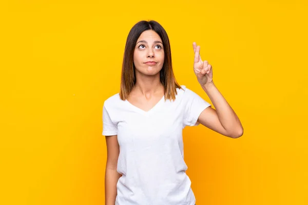 Jovem Mulher Sobre Fundo Amarelo Isolado Com Dedos Cruzando Desejando — Fotografia de Stock