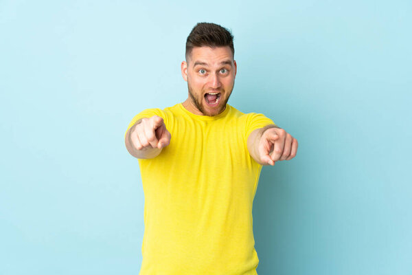 Russian handsome man isolated on blue background surprised and pointing front