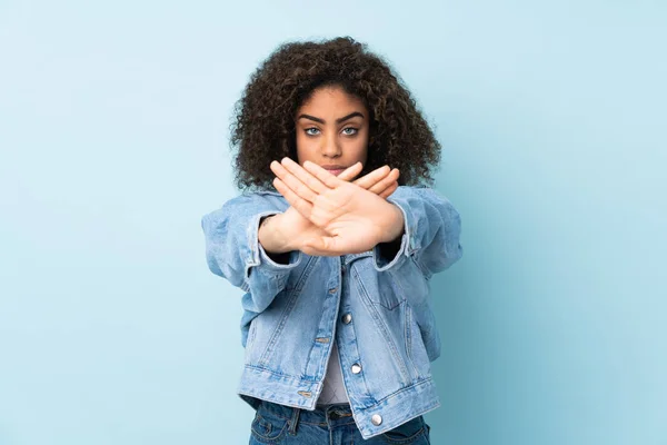 Young African American woman isolated on blue background making stop gesture with her hand to stop an act