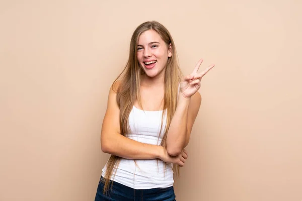 ティーンブロンド女の子上の隔離された背景笑顔とショー勝利サイン — ストック写真