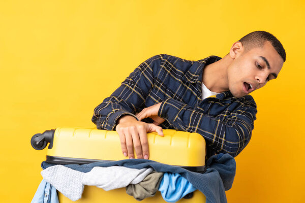 Traveler man with a suitcase full of clothes over isolated yellow background