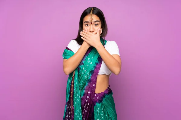 Young Indian woman with sari over isolated background covering mouth with hands