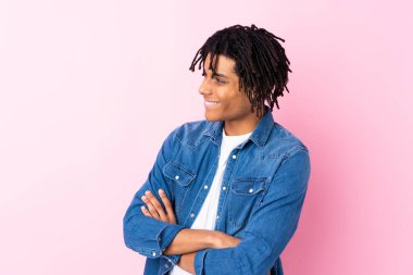 Soyutlanmış pembe arka planda kot gömlekli genç Afrikalı Amerikalı bir adam yan tarafa bakıyor.