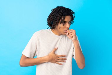 İzole edilmiş mavi arka plandaki genç Afrikalı Amerikalı adam öksürük ve kötü hissetmekten muzdarip.