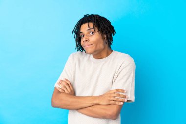 Genç Afrikalı Amerikalı bir adam mavi arka planda, omuzlarını kaldırırken şüpheyle hareket ediyor.