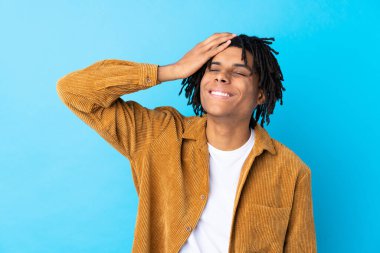 Kadife ceketli genç Afro-Amerikalı adam mavi arka planda gülüyor.