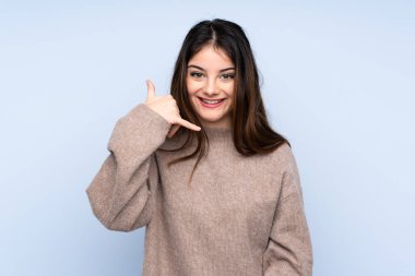 Genç esmer kadın, izole edilmiş mavi arka plan üzerine kazak giyip telefon jesti yapıyor. Bana geri dönüş işareti ver.