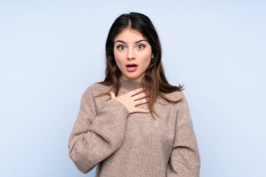 İzole edilmiş mavi arka planda süveter giyen genç esmer kadın sağa bakarken şaşırmış ve şok olmuştu.