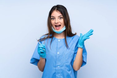 Kadın dişçi aletleri kapalı kapalı mavi arka plan üzerinde şaşırtıcı yüz ifadesi ile