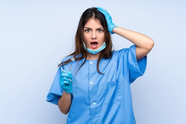 Kadın dişçi aletleri kapalı kapalı mavi arka plan üzerinde şaşırtıcı yüz ifadesi ile