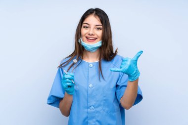 İzole edilmiş mavi arkaplan üzerinde aletleri tutan kadın diş hekimi telefon hareketi yapıyor