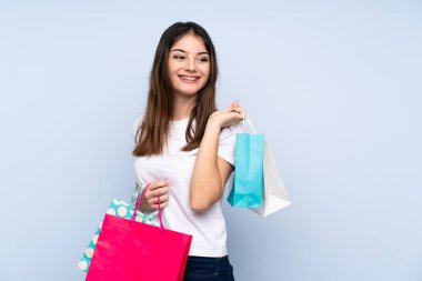 Genç esmer kadın izole edilmiş mavi arka planda alışveriş torbaları tutuyor ve gülümsüyor.