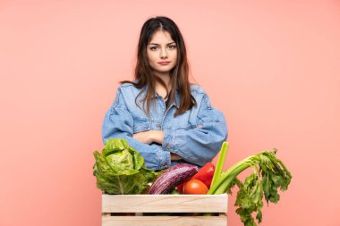 Genç çiftçi kadın elinde bir sepet dolusu taze sebzeyle kollarını kavuşturuyor.