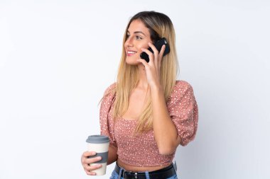 Genç Uruguaylı kadın izole edilmiş beyaz arka planda elinde kahve ve bir cep telefonu tutuyor.