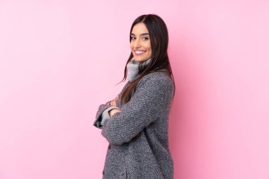 Genç esmer kadın pembe arka planda, kolları bağlı ve ileriye bakıyor.