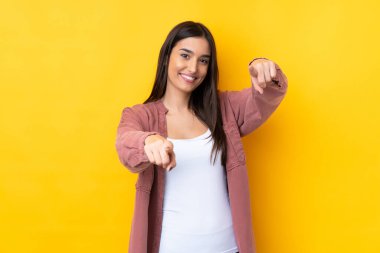 Sarı arka plandaki genç esmer kadın gülümserken seni işaret ediyor.